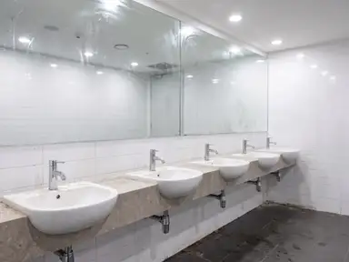 Commercial restroom overdue for a deep clean, limescaled chrome, a hazed mirror and darkened grout