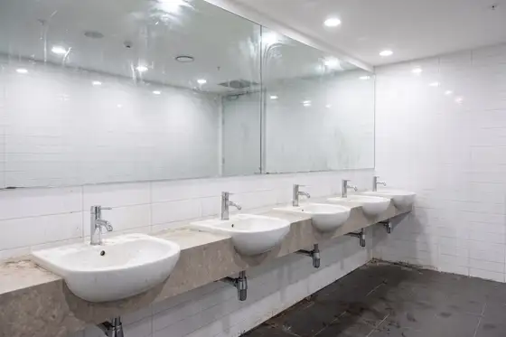 Commercial restroom fixture and tile showing mineral scale and staining at the grout line