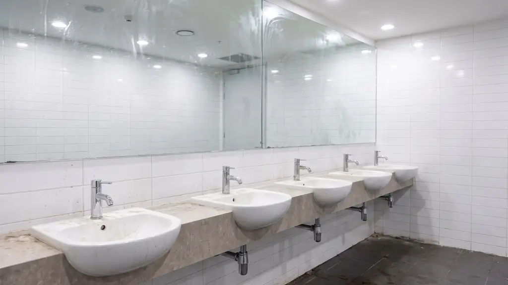 Commercial restroom fixture and tile showing mineral scale and staining at the grout line