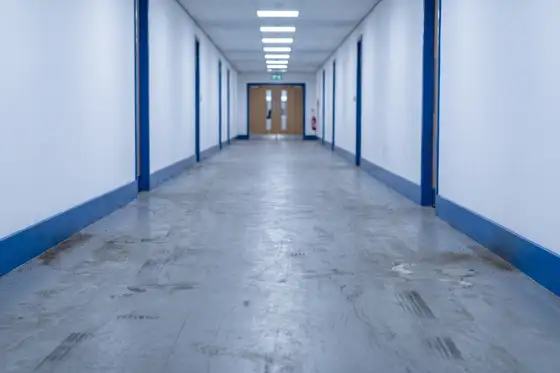 Scuffed and black-marked vinyl corridor floor under raking light before restoration