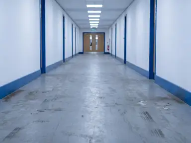 Commercial corridor floor before a scrubber pass, gray and hazed with black heel marks along the base