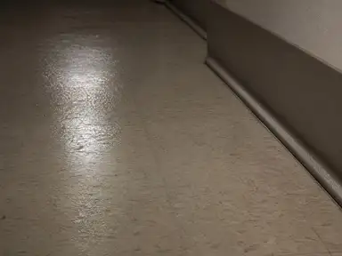 Damp-mopped vinyl corridor floor drying under night lighting in a commercial building