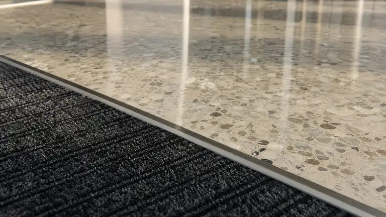 Walk-off mat meeting a polished terrazzo lobby threshold in daylight