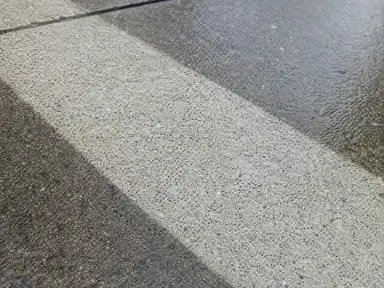 Pressure-washed clean stripe cut across a weathered commercial concrete sidewalk