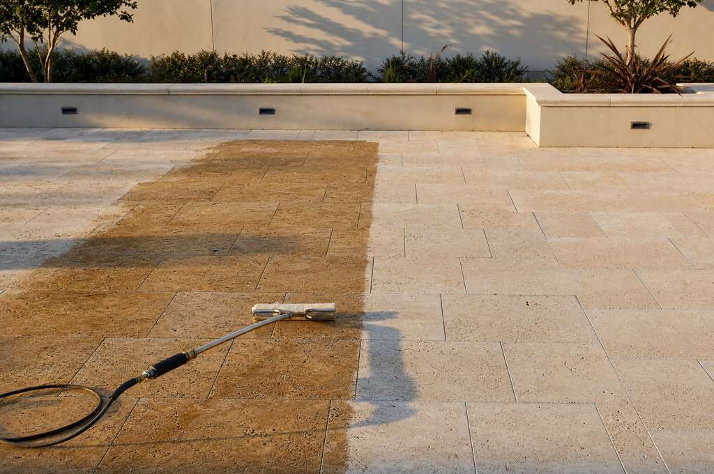 Wet-look sealer freshly applied across travertine pavers, meeting the dry unsealed stone along a clean edge