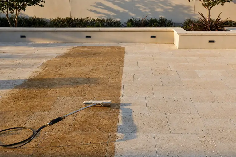 Wet-look sealer freshly applied across travertine pavers, meeting the dry unsealed stone along a clean edge
