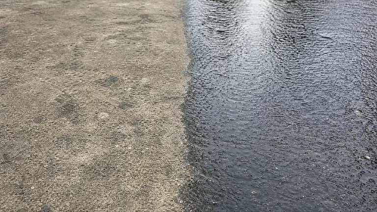Worn traffic lane in a concrete sealer beside a freshly resealed glossy section