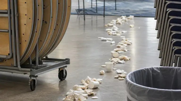 Banquet hall part-way through a turnaround, tables folded onto a dolly and debris swept into a line