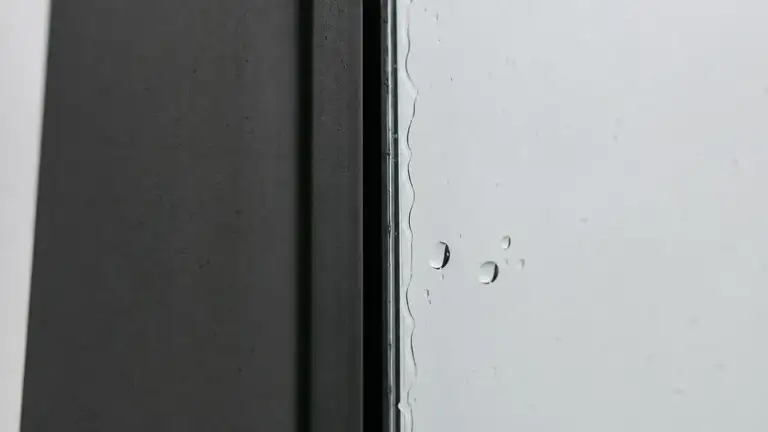Squeegeed commercial glass pane meeting an aluminum mullion, water line at the edge
