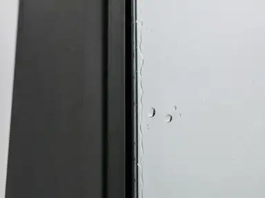 Squeegeed commercial glass pane meeting an aluminum mullion, water line at the edge