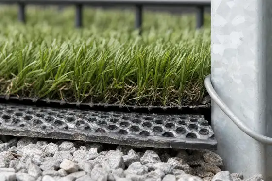 Artificial turf lifted at the edge to show perforated drainage backing and infill layer