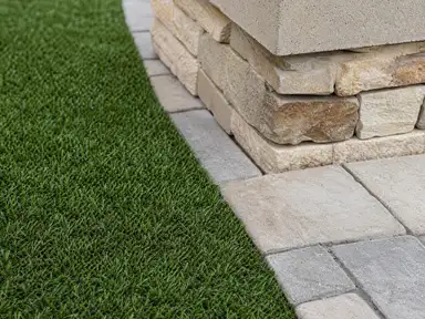 Artificial turf meeting a paver patio edge beside a planter base