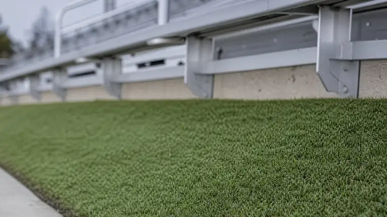 Artificial turf on a spectator bank meeting the concrete footing of aluminum bleachers